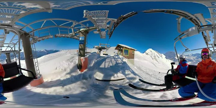 360VR two male skiers going up mountain with chair ski lift on sunny winter day with clear blue sky starting their skiing day in amazing snow covered mountain range skiing region
