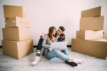 Young couple moving in a new home. Man and woman with notebook laptop computer and boxes in empty room.