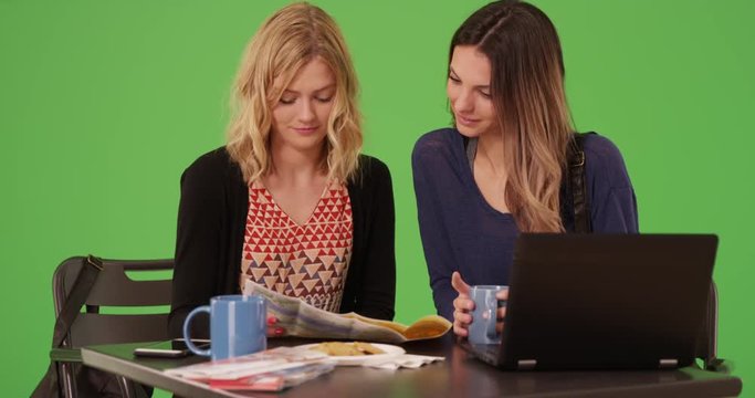 Two beautiful young woman with travel map and laptop indoors greenscreen studio