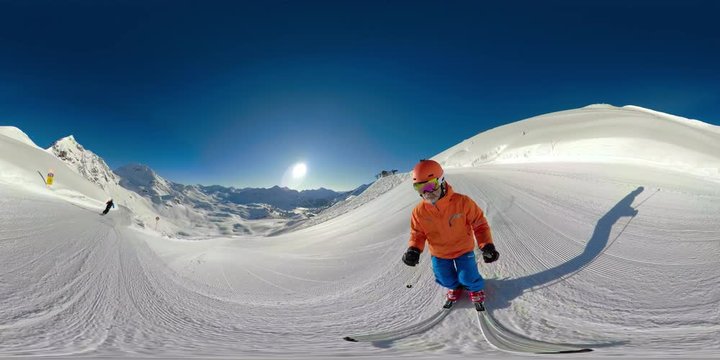 360VR two skiers skiing on sunny winter vacation day in mountains with clear blue sky on ski slope and in deep snow one falling at the end
