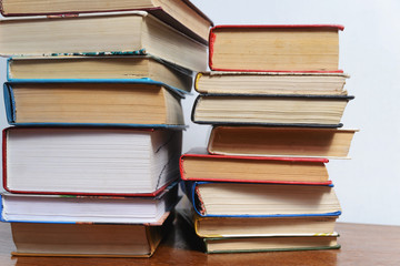 Stack of different books on a table against a white wall background