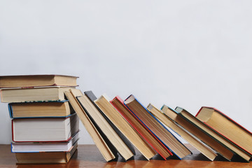 Stack of different books on a table against a white wall background