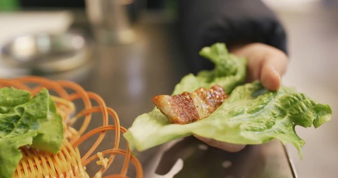 Woman wrapping grilled korean meat in lettuce at restaurant