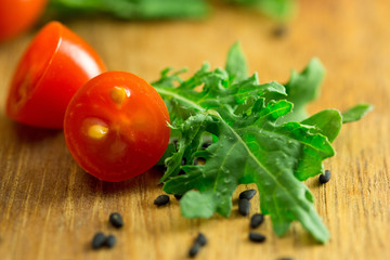 Cherry tomatoes black sesame seeds and baby kale in macro on wooden cutting board