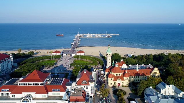 Sopot resort in Poland. Vacation infrastructure with spa, old lighthouse, wooden pier (molo), promenade, marina, yachts, ship and beach. Aerial 4K flyby video in sunset light