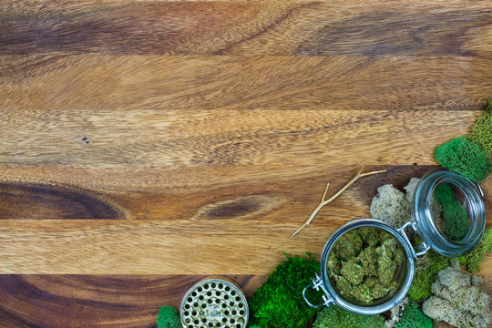 Marijuana in glass jar surrounded by moss and grinder with wooden background