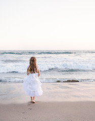Young girl wearing a white dress walking on the beach  towards the ocean
