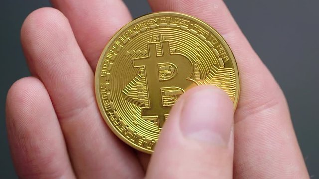 Closeup of hand holding a bitcoin and running a thumb across it
