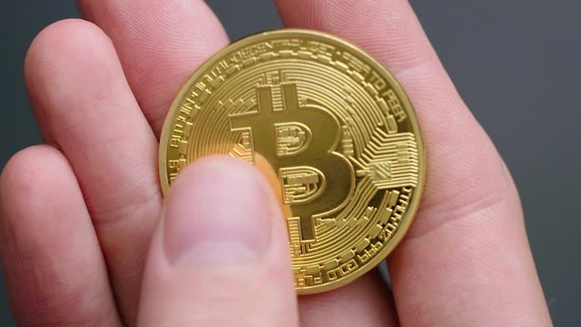 Closeup of caucasian hand holding and feeling a gold bitcoin