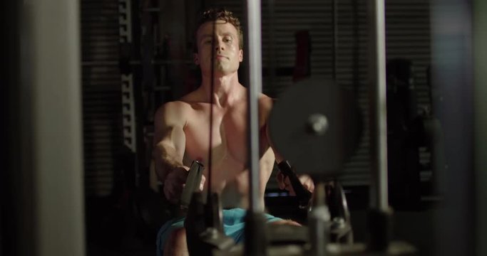 Male athlete does one handed rows on workout machine
