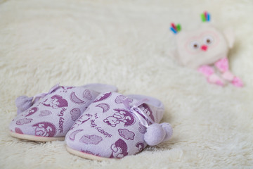 a handmade little owl toy and a child's lilac slippers on a white furry plaid as a background