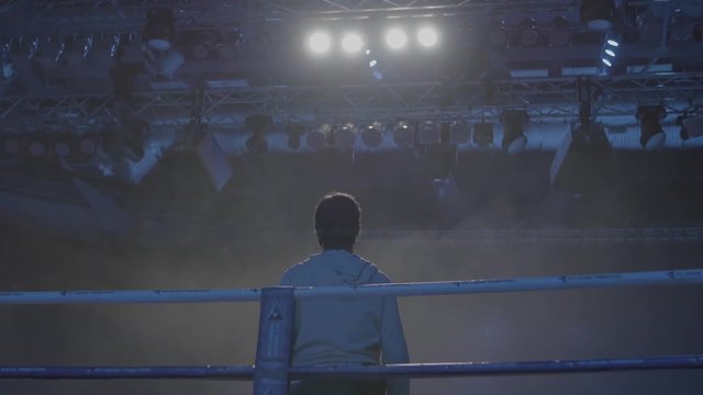 Back view of working gaffer or lighting technician and spotlights background. Lighting technician, placing the light during a film. Lighting technicians operating strobes during a concert