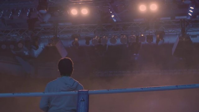 Back view of working gaffer or lighting technician and spotlights background. Lighting technician, placing the light during a film. Lighting technicians operating strobes during a concert