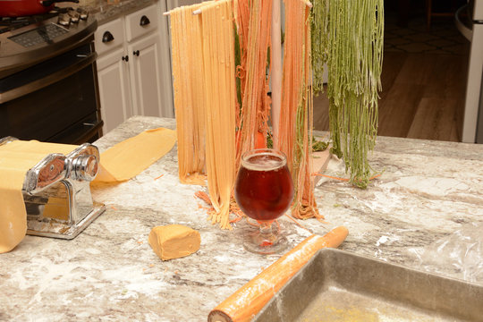 Glass of cold beer in front of drying home made pasta on wooden tree rack