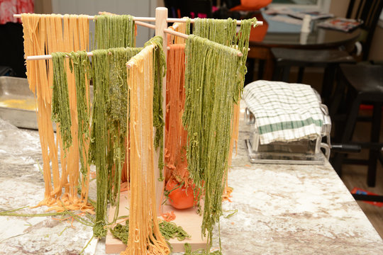Colorful red and green fresh made pasta drying on wooden tree rack