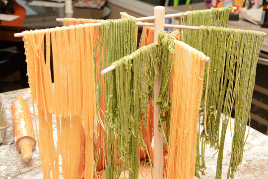 Colorful red and green fresh made pasta drying on wooden tree rack