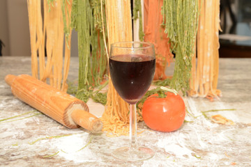 Glass of wine in front of pasta drying on wooden tree rack