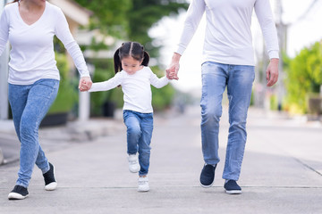 Parents and daughter are holding hands. Kid  going in the park.Young family with little girl having fun in nature.