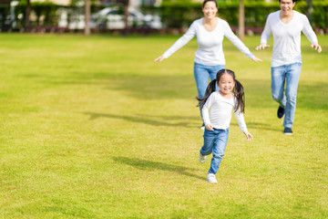 Obraz premium Little girl is running with parents in the park. Young family with little kid having fun in nature.