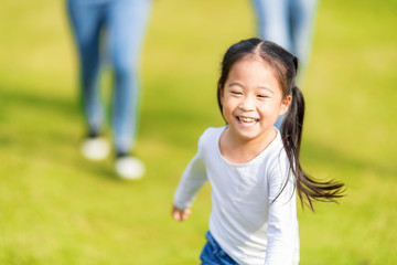 Little girl is running with parents in the park. Young family with little kid having fun in nature.