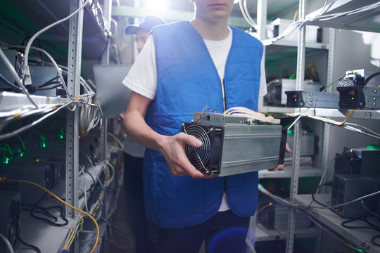 Mining. A man works on a cryptocurrency farm. Holds bitcoin mining equipment in hand