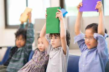Happy Four of Children Sitting on Chair with a Book in hand in Library. Development of Human Resources in Education Concept. Setup studio shooting.