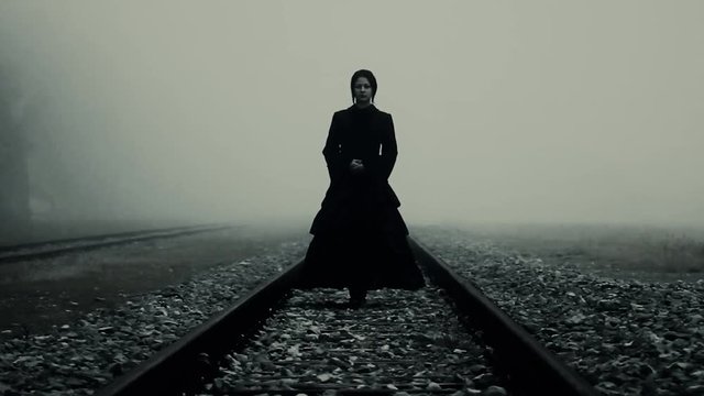 Horror scene of a terrifying woman in black dress staying at trails in the fog