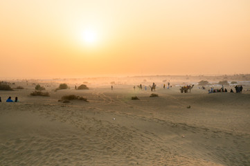 Fototapeta na wymiar Foggy sunset in the thar desert in Rajasthan with people and camels visible on the horizon. Sum is a very famous tourist destination