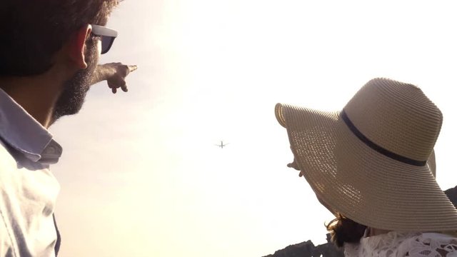 Young couple pointing airplane in the sky beautiful girl with hat man boyfriend wearing sunglasses slow motion