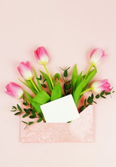 A bouquet of beautiful pink tulips in a pink envelope and a card for text on a pale pink background. Holiday background.Top view. Copy space