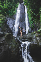Woman enjoying near hidden in jungle cascade waterfall in Bali. Slim body and black swimsuit, fashion model. Dusun Kuning in Ubud area