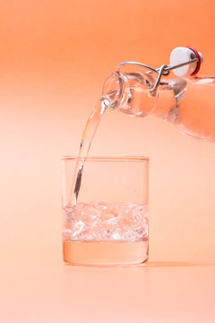 Pouring water from bottle to glass on orange background