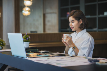 Businesswoman working on laptop while drinking coffee in the office