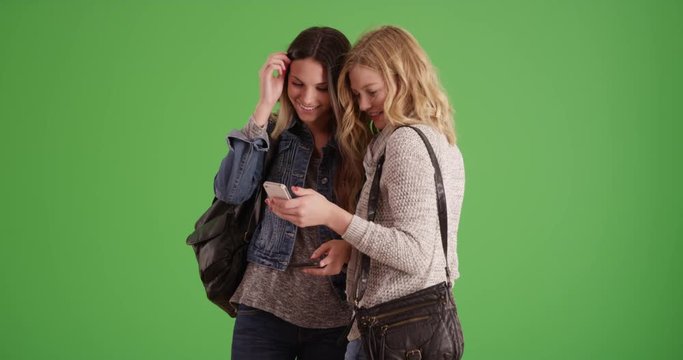 Couple young caucasian women looking at smartphone on greenscreen