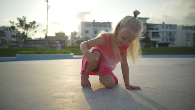 Blonde baby girl draw chalk on the playground at sunrise rapid slow motion