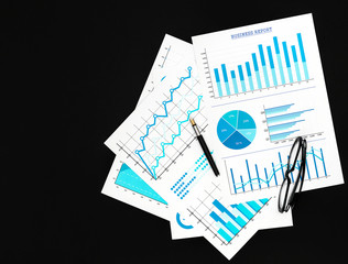 Financial graphs with pen and eyeglasses on the black background. Top view. Copy space.