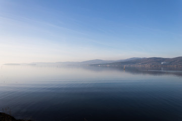 Fototapeta premium Beautiful view of Trasimeno lake (Umbria, Italy), with hills and blue sky reflecting on water