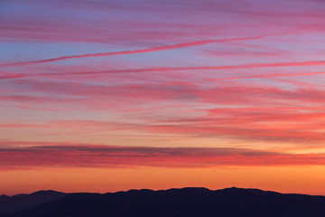 Clouds and jet vapor trails creating beautiful, colorful texture in the sky at sunset with mountain profiles on the low part of the frame