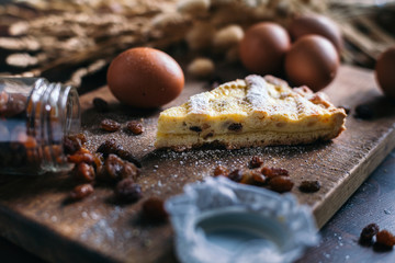 Traditional italian cake with ricotta cheese and raisin, eggs, jar and powdered sugar on wooden...