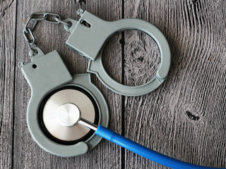 medical stethoscope and handcuffs on wooden background