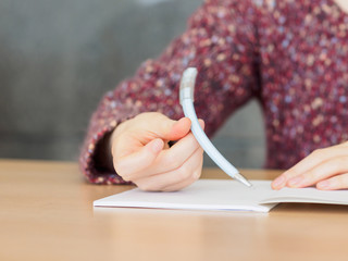 Close up of woman's hands rotating a pen with notepad placed on wooden table.