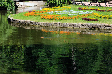 Fototapeta na wymiar Summer park, lake and flowerbed on lawn.
