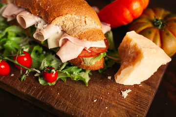 Traditional italian sandwich with cheese, ham, salad, tomatoes and parmesan on wooden background, selective focus