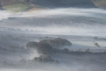 Stunning foggy English rural landscape at sunrise in Winter with layers rolling through the fields