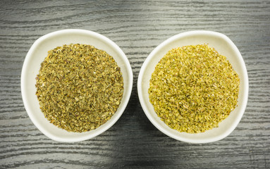 White bowls with dried basil and oregano on a dark table. View from above.