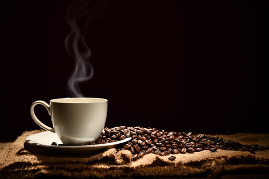Fototapeta Filiżanka kawy z dymnymi i kawowymi fasolami na czarnym tle