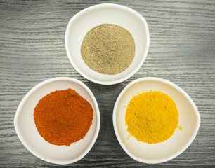 A set of three white bowls with spices - pepper, paprika and curry. View from above.
