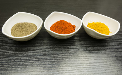 Three white bowls with spices - black pepper, paprika and curry.