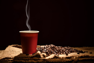 Paper cup of coffee with smoke and coffee beans on black background