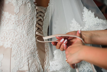 Obraz na płótnie Canvas bridesmaid hands lace up white wedding dress on the back
